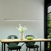 Moderne, slanke LED-hanglamp in zilver boven een houten tafel met twee groene stoelen, een vaas met witte bloemen en een fruitschaal; perspectief: vooraanzicht op ooghoogte.