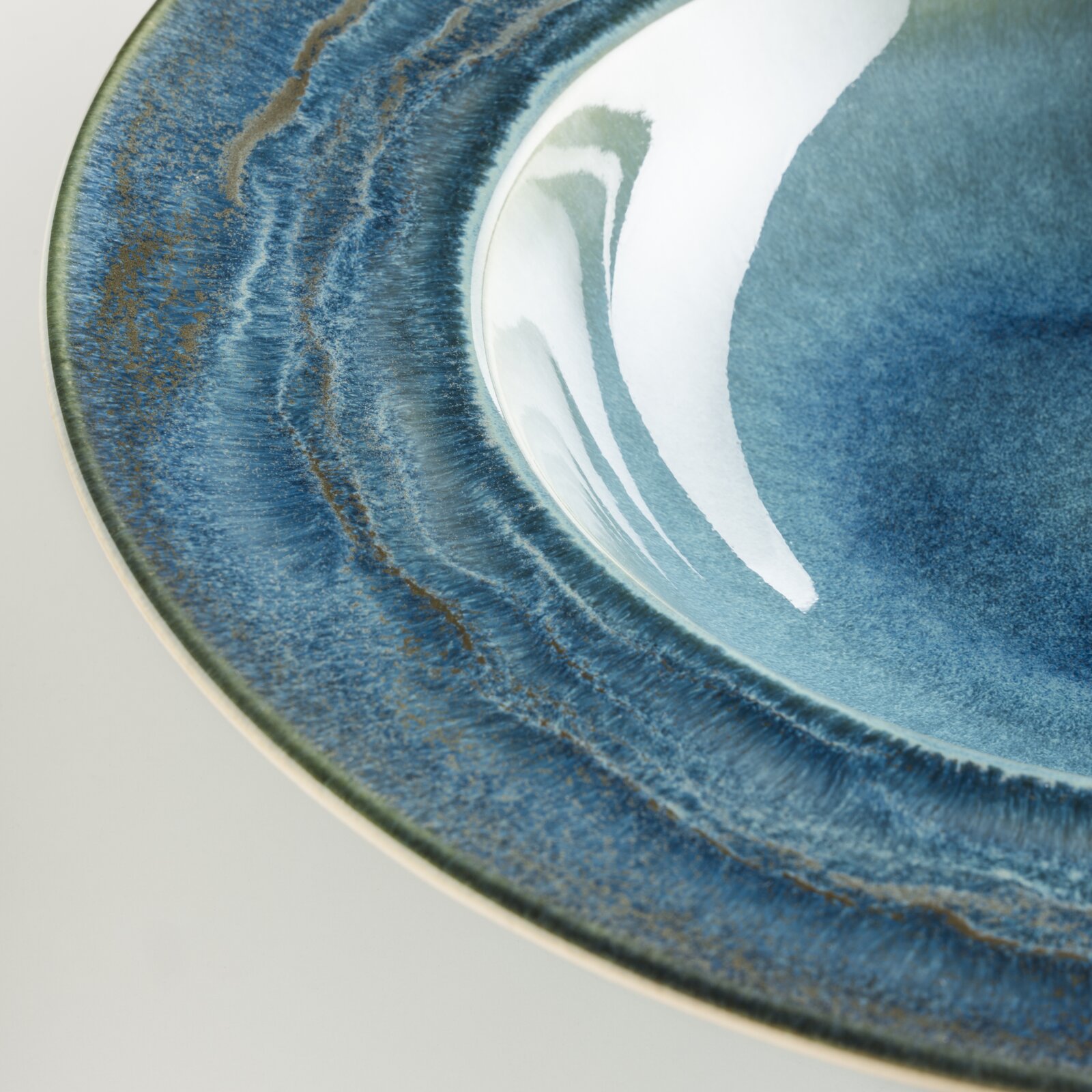 Detailaufnahme eines runden, blau glasierten Keramiktellers mit strukturierter, leicht marmorierter Oberfläche und glänzender Innenfläche, schräg von oben fotografiert