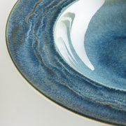 Detailaufnahme eines runden, blau glasierten Keramiktellers mit strukturierter, leicht marmorierter Oberfläche und glänzender Innenfläche, schräg von oben fotografiert