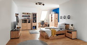 Modernes Schlafzimmer mit Holzmöbeln, darunter ein Bett mit Stauraum, ein Schreibtisch mit Stuhl und ein Kleiderschrank, aus der Perspektive von der Zimmerecke aus gesehen.