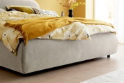 Zijaanzicht van een grijs gestoffeerd bedframe LISSABON met een gele deken en kussens met patroon.