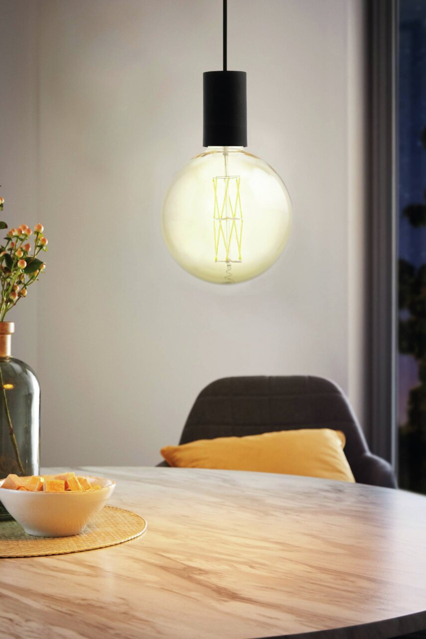 Moderne Pendelleuchte POZUETA mit großer Glühbirne, hängend über einem Tisch in einem gemütlichen Raum, seitliche Perspektive.