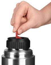 Nahaufnahme einer Hand, die den Verschluss einer silbernen Isolierflasche mit schwarzem Deckel und rotem Hebel öffnet.