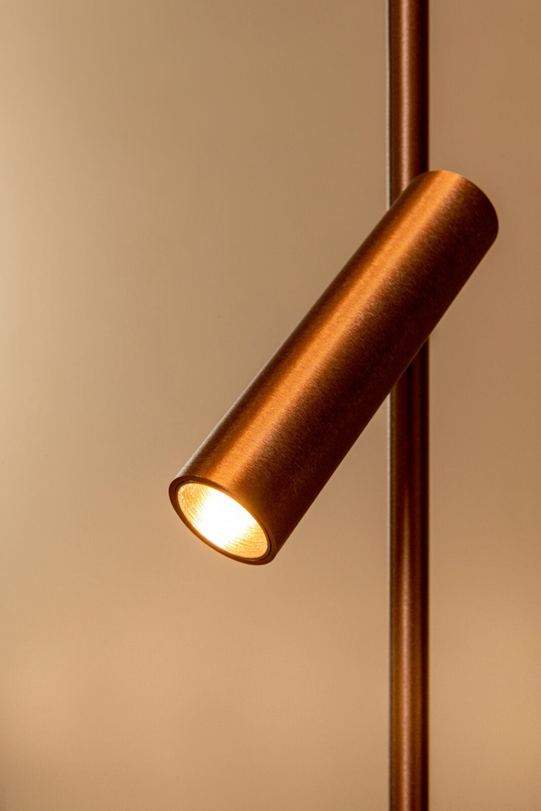 Nahaufnahme eines zylindrischen LED-Spots in gebürsteter Kupfer-/Bronzeoptik an einer vertikalen Stange, warm leuchtend, schräg von vorne/seitlich fotografiert