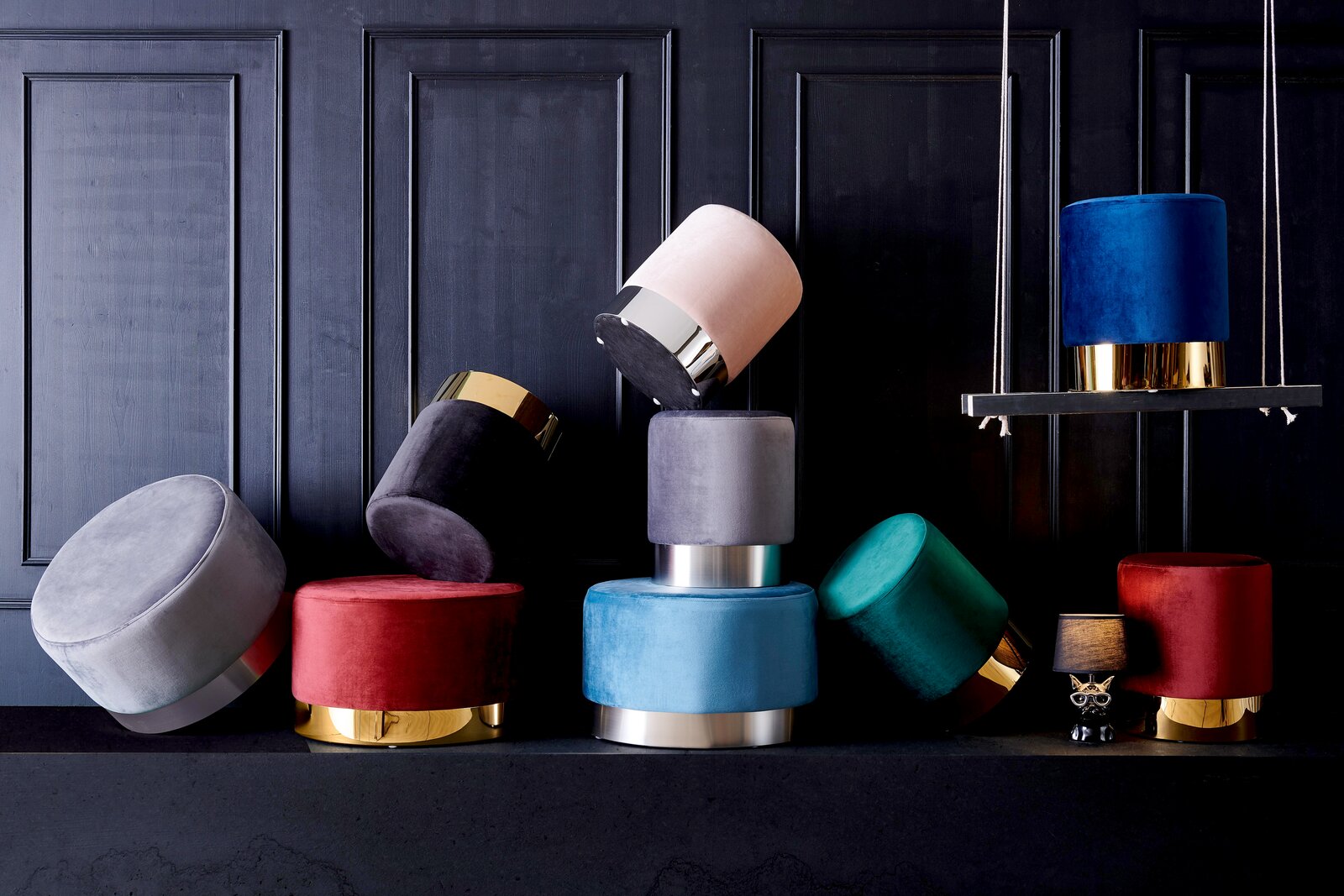 Eine Sammlung von bunten, runden Hockern der Serie XORA PURO, die auf einem dunklen Hintergrund gestapelt und arrangiert sind. Die Hocker haben metallische Akzente und sind in verschiedenen Farben wie Blau, Rot, Grün und Grau erhältlich. Perspektive: Fron