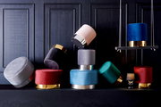Eine Sammlung von bunten, runden Hockern der Serie XORA PURO, die auf einem dunklen Hintergrund gestapelt und arrangiert sind. Die Hocker haben metallische Akzente und sind in verschiedenen Farben wie Blau, Rot, Grün und Grau erhältlich. Perspektive: Fron