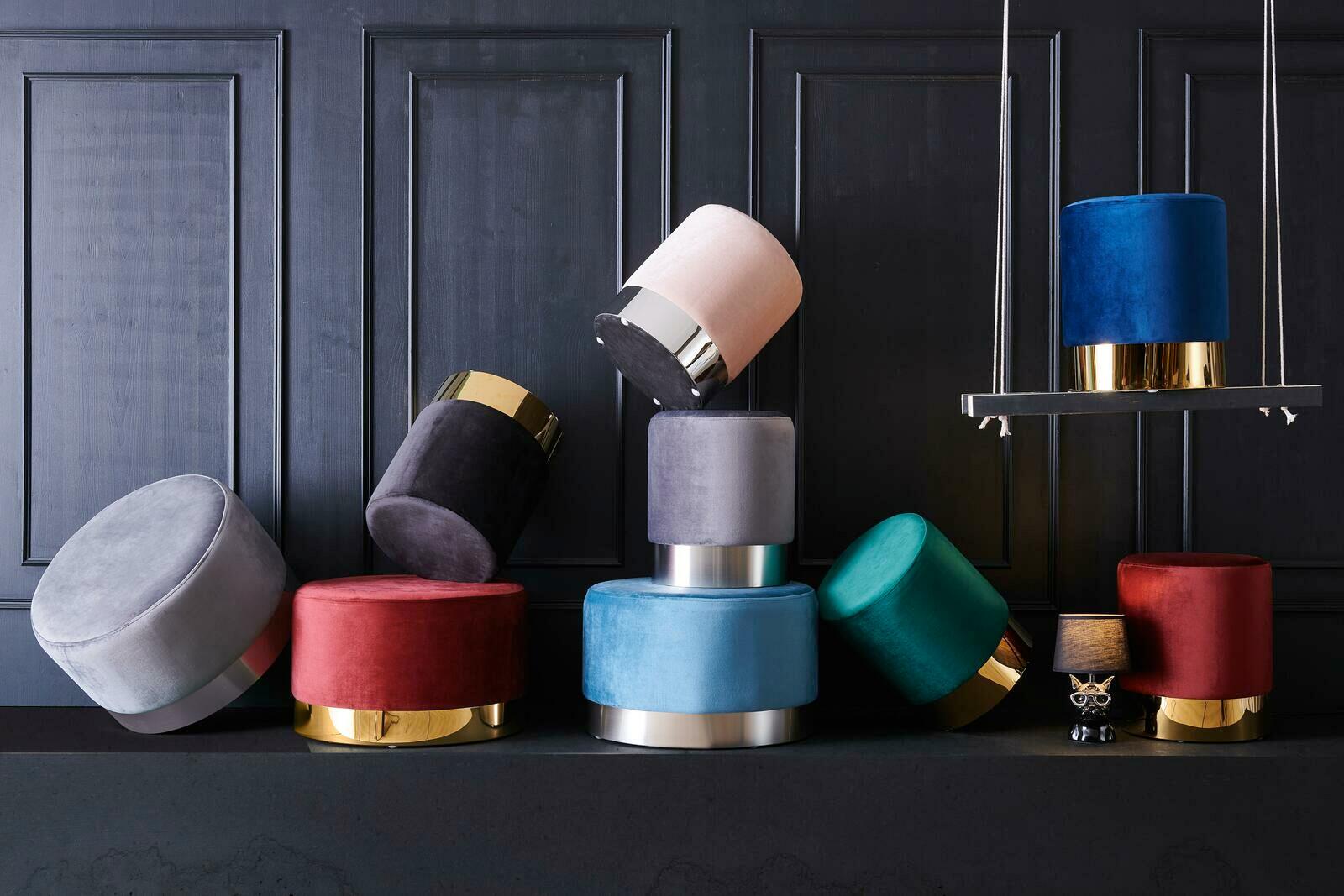 Eine Sammlung von bunten, runden Hockern der Serie XORA PURO, die auf einem dunklen Hintergrund gestapelt und arrangiert sind. Die Hocker haben metallische Akzente und sind in verschiedenen Farben wie Blau, Rot, Grün und Grau erhältlich. Perspektive: Fron