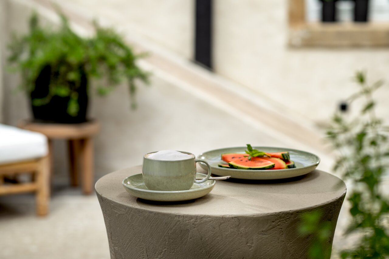 Like by Villeroy & Boch Untertasse PERLEMOR ALGA Kaffeeuntertasse mit Tasse und Schaum, auf einem Tisch im Freien, seitliche Perspektive