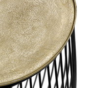 Nahaufnahme eines Beistelltisches mit goldener, strukturierter Oberfläche und schwarzem Drahtgestell, von oben betrachtet.