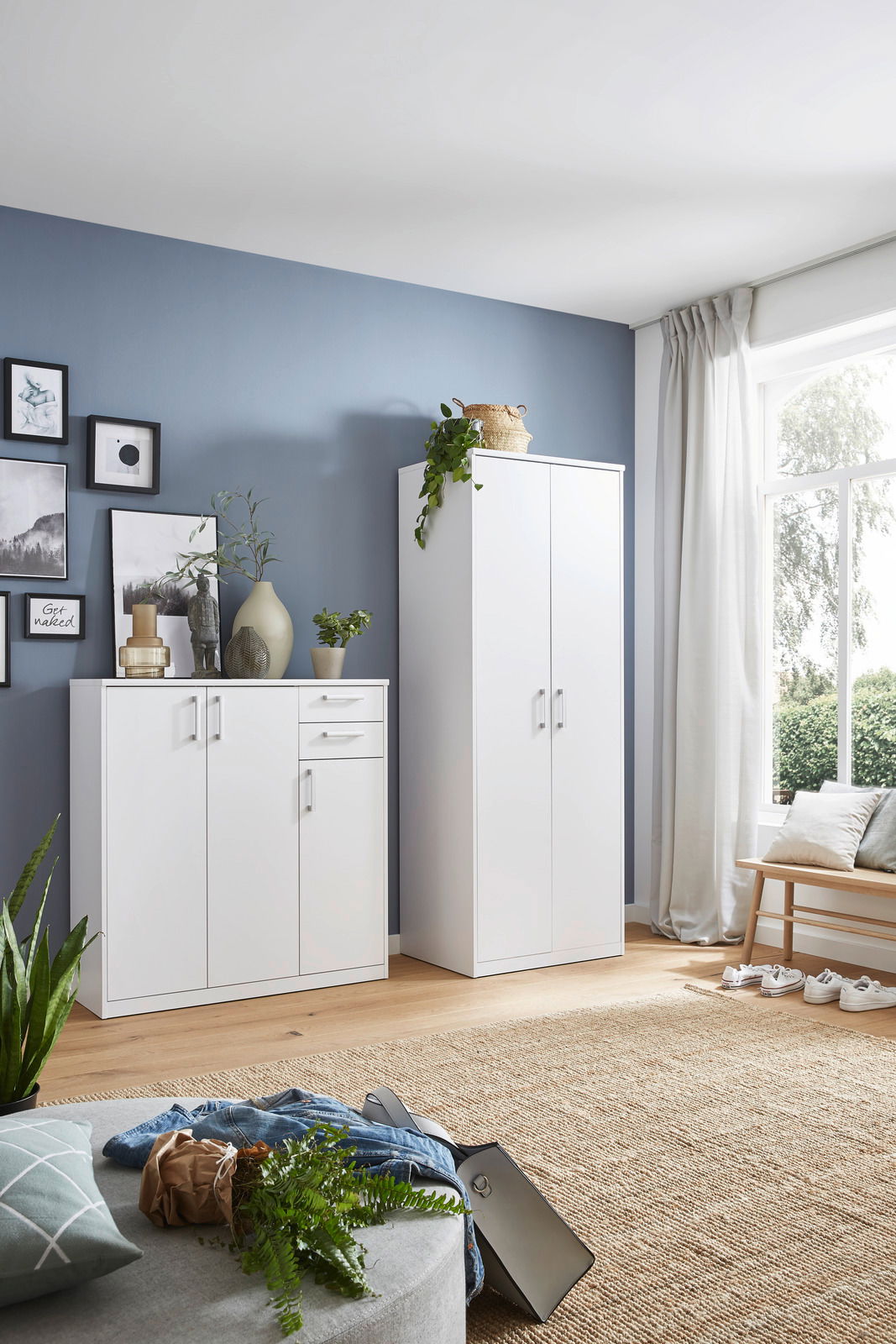 Weiße Schränke in einem modernen Wohnzimmer mit blauer Wand und großem Fenster, seitliche Perspektive.