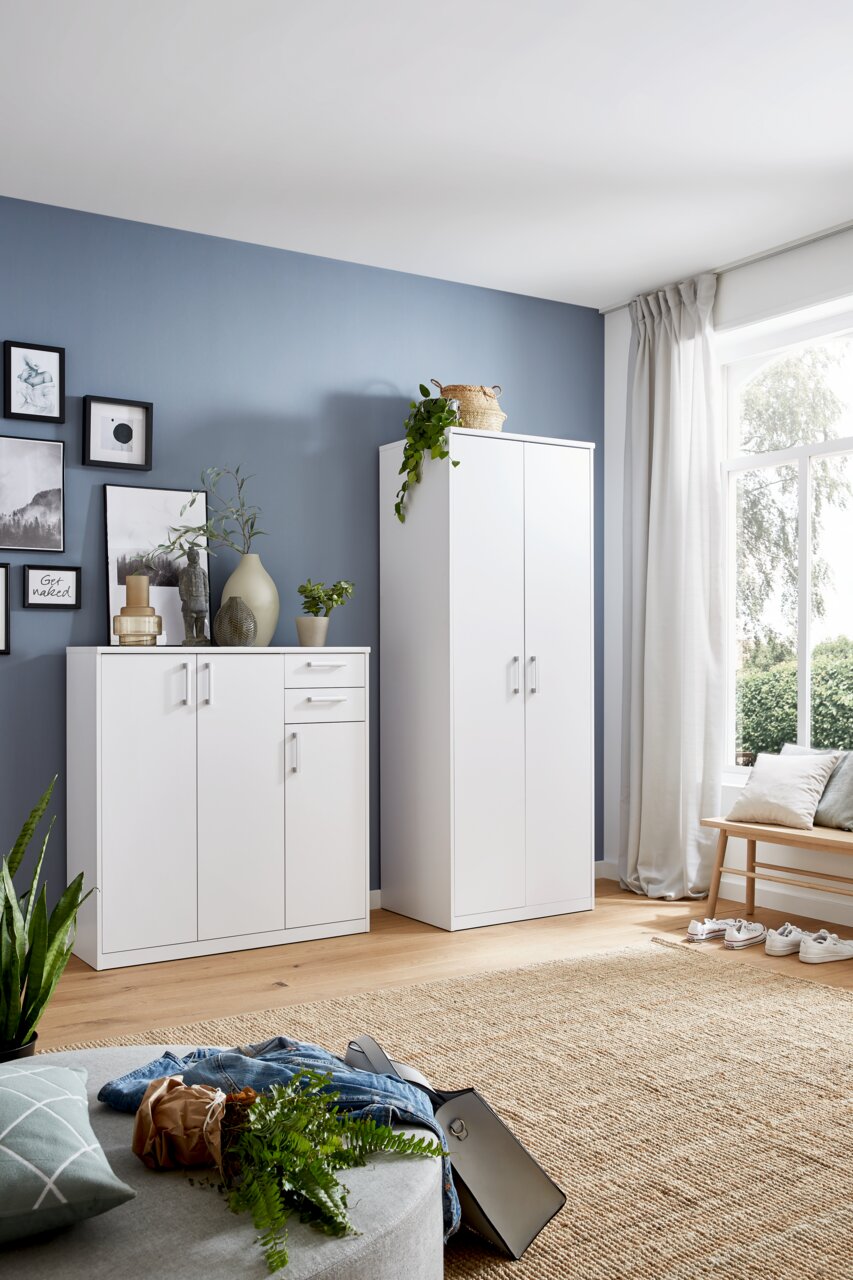 Weiße Schränke in einem modernen Wohnzimmer mit blauer Wand und großem Fenster, seitliche Perspektive.