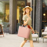 Frau mit Strohhut und grünem Kleid trägt eine rosa Multibag Style 25l Tasche, seitliche Perspektive, draußen in urbaner Umgebung.