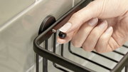 Nahaufnahme eines schwarzen Eckduschkorbs von tesa ALUXX, der an einer Wand montiert wird. Eine Hand hält eine Schraube zur Befestigung.