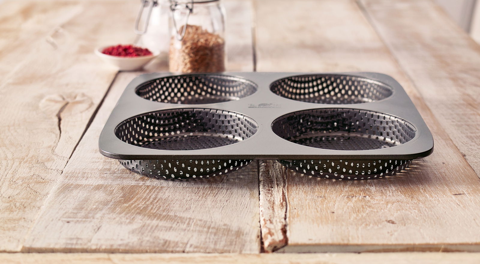 Birkmann Burger-Brötchenblech Burger Brötchen-Blech mit vier runden Formen, auf einem Holztisch von der Seite fotografiert.