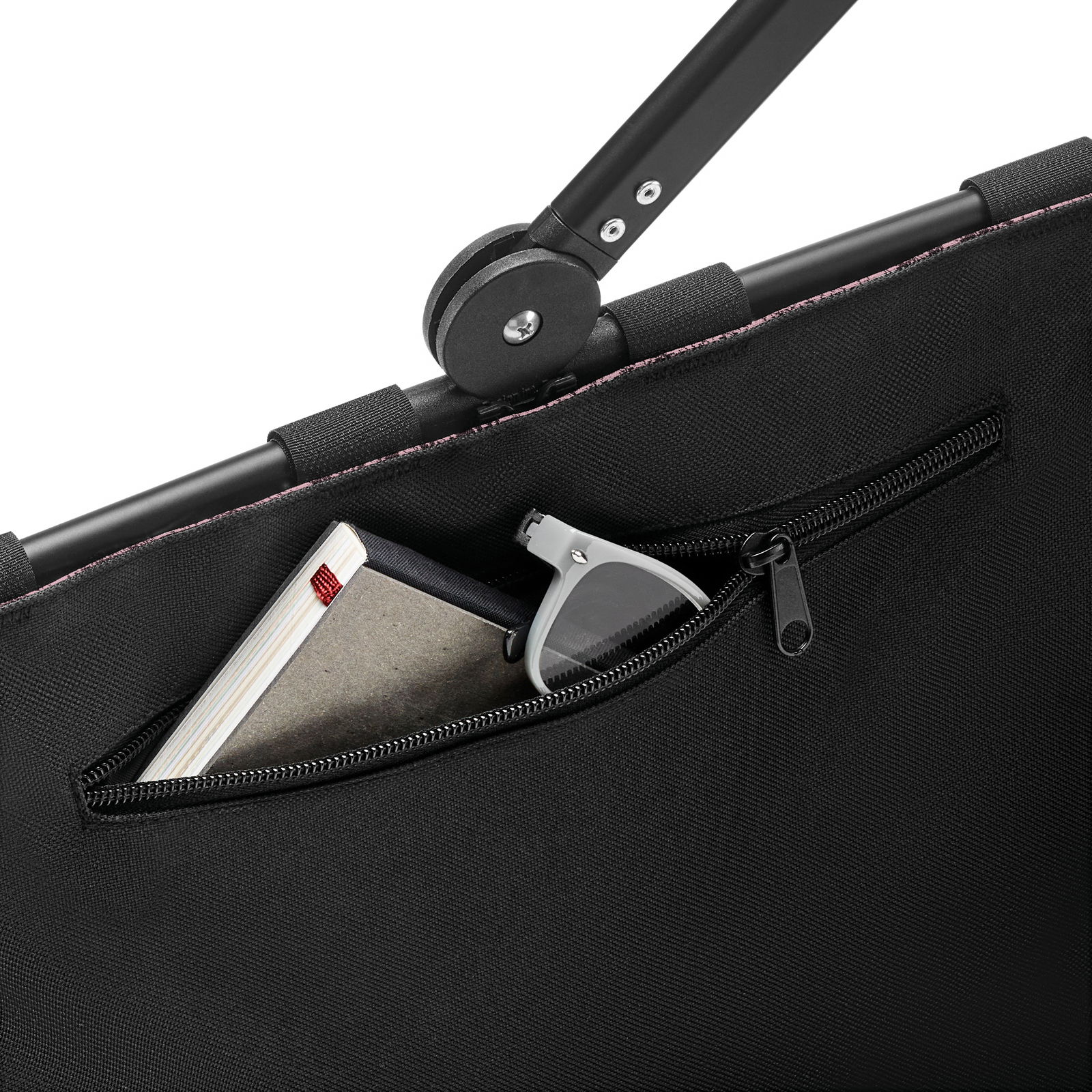 Nahaufnahme einer schwarzen Tragetasche mit Reißverschlussfach, das eine Sonnenbrille und ein Notizbuch enthält.