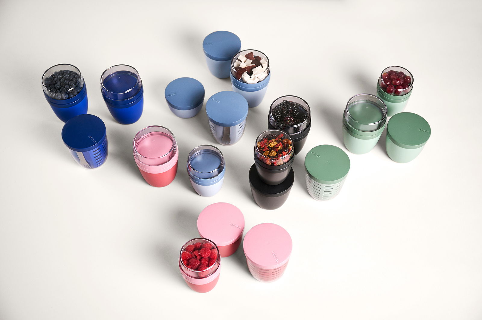Verschiedene bunte Fruchtbehälter in elliptischer Form, gefüllt mit Beeren und anderen Früchten, aus der Vogelperspektive.