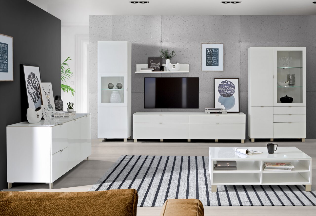 Moderne Wohnzimmermöbel in Weiß, bestehend aus einem TV-Lowboard, Hängeschränken, Vitrinen und einem Couchtisch, aus der Perspektive eines gemütlichen Wohnzimmers.