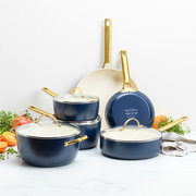 Set aus blauen Bratpfannen und Töpfen mit goldenen Griffen, auf einer weißen Oberfläche arrangiert, mit Blick von vorne.