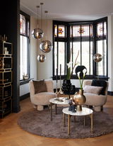 Moderne Hängeleuchte mit drei kugelförmigen, rauchgrauen Glaskörpern in einem stilvollen Wohnzimmer mit großen Fenstern und eleganter Dekoration, seitliche Perspektive.