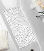 Blick von oben auf eine Wanneneinlage mit Kieselstein-Optik in einer weißen Badewanne, umgeben von Handtüchern und Pflegeprodukten.