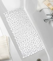 Blick von oben auf eine Wanneneinlage mit Kieselstein-Optik in einer weißen Badewanne, umgeben von Handtüchern und Pflegeprodukten.