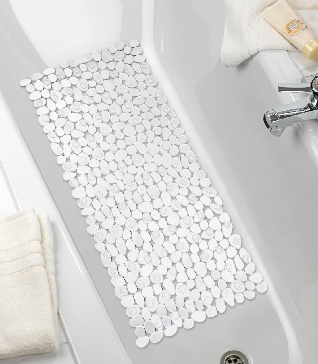 Blick von oben auf eine Wanneneinlage mit Kieselstein-Optik in einer weißen Badewanne, umgeben von Handtüchern und Pflegeprodukten.