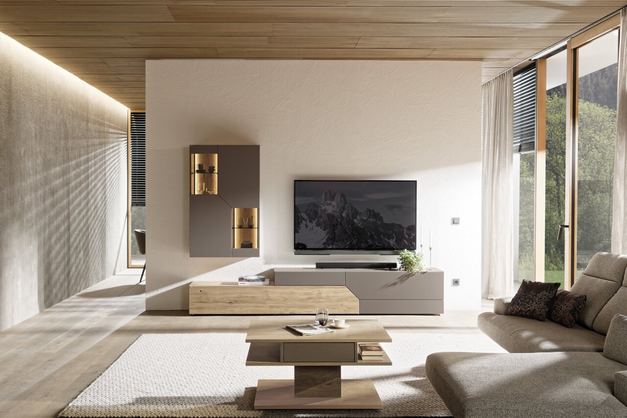 Modernes Wohnzimmer mit TV-Wand, schwebendem Lowboard in Grau und Holz sowie beleuchteter Vitrine; frontale Perspektive auf die Wohnwand