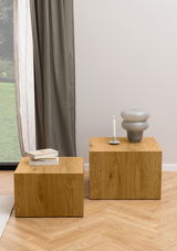 Zwei moderne, kubische Couchtische aus Holz in einem Wohnzimmer, einer mit Büchern und der andere mit einer Kerze und einer Vase dekoriert. Seitliche Perspektive.