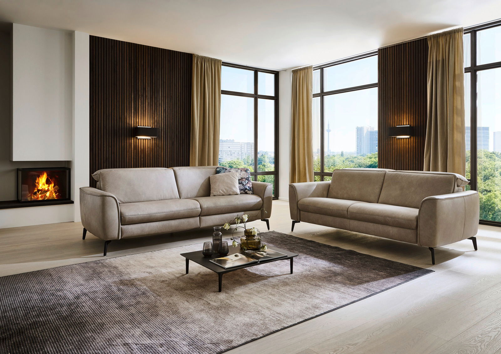 Modernes Wohnzimmer mit zwei beigen Sofas, einem niedrigen Couchtisch und einem Kamin im Hintergrund. Große Fenster bieten einen Blick auf die Stadt. Perspektive von vorne.