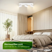 Witte plafondspot met drie verstelbare lampkoppen en warmwit licht in een moderne slaapkamer, gezien van onderen in een ruim interieurperspectief.