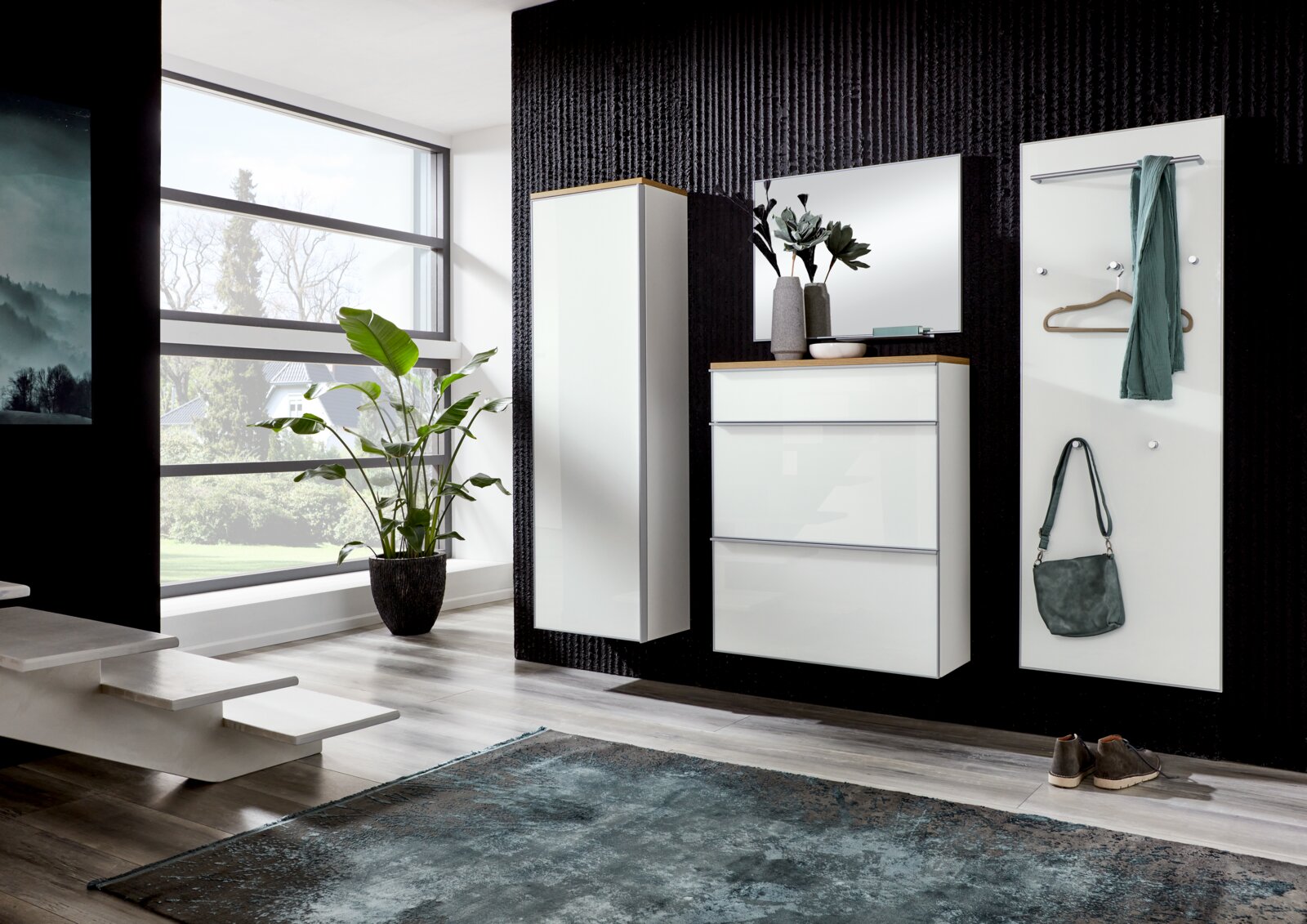 Modernes Flur-Set mit weißer Hochglanz-Garderobe: hoher Schrank, Schuhschrank mit Spiegel und Garderobenpaneel mit Haken, aufgenommen in frontaler Perspektive leicht von links in einem hellen Eingangsbereich.