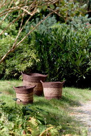 Drei geflochtene Körbe aus Naturmaterialien auf einer Wiese im Garten, seitliche Perspektive.