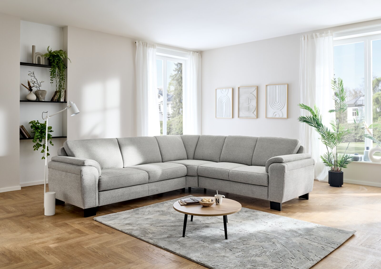 Beldomo System Ecksofa OSAKA-S Hellgraues L-förmiges Ecksofa mit gepolsterten Armlehnen in einem hellen Wohnzimmer mit Couchtisch und Teppich, Perspektive: frontale Weitwinkelansicht leicht von links.