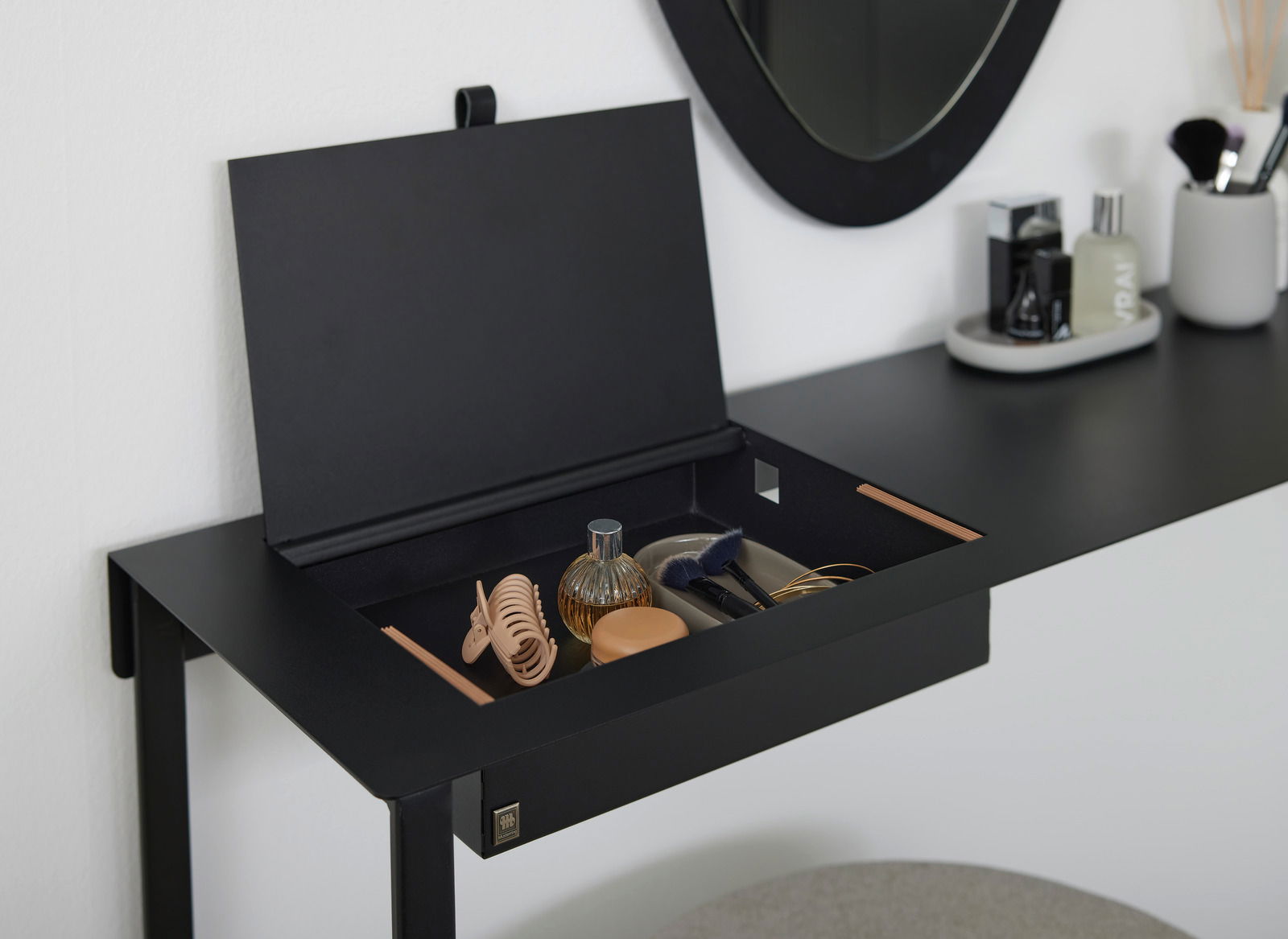 Schwarzer Konsolentisch mit geöffnetem Fach, das verschiedene Accessoires enthält, seitliche Perspektive.