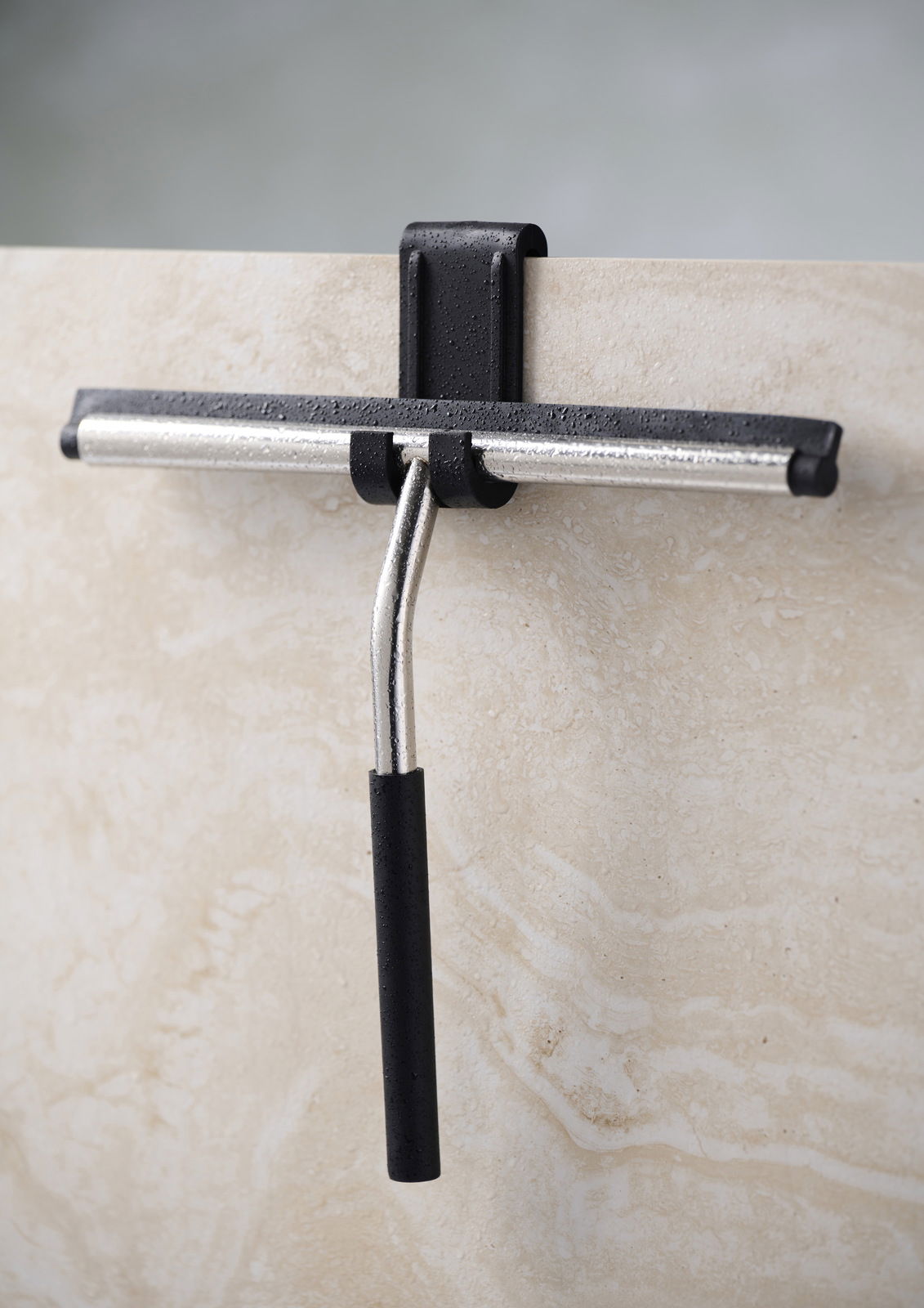 Badabstreifer mit Aufhängung, frontal an einer Duschwand befestigt, mit schwarzem Griff und Metallstange.