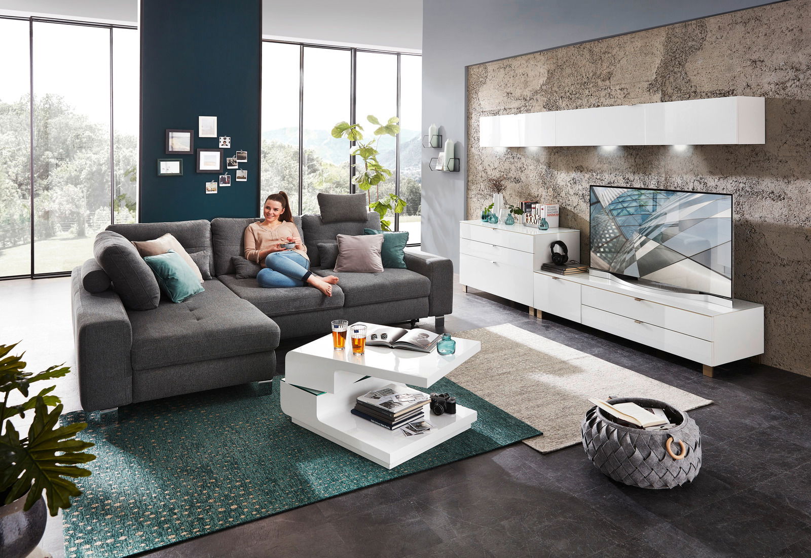 Moderne Wohnzimmeransicht mit grauem Ecksofa, weißem Funktions-Couchtisch und stilvollem Hängeschrank an der Wand.