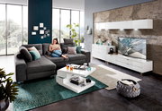 Moderne Wohnzimmeransicht mit grauem Ecksofa, weißem Funktions-Couchtisch und stilvollem Hängeschrank an der Wand.