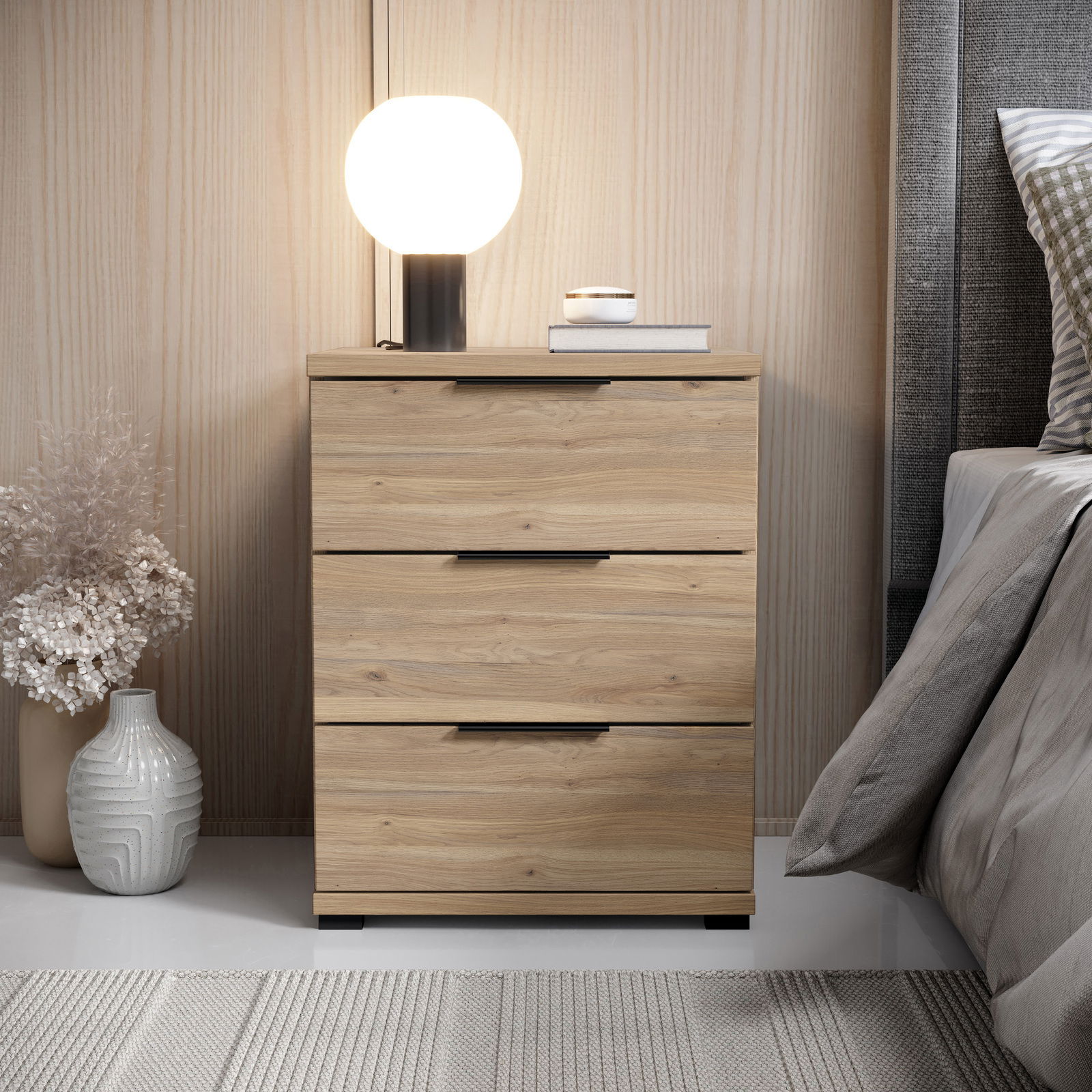 Z2 Nachtkommode SMILLA 2 Nachtkommode aus Holz mit drei Schubladen, darauf eine runde Lampe und Bücher, seitliche Perspektive
