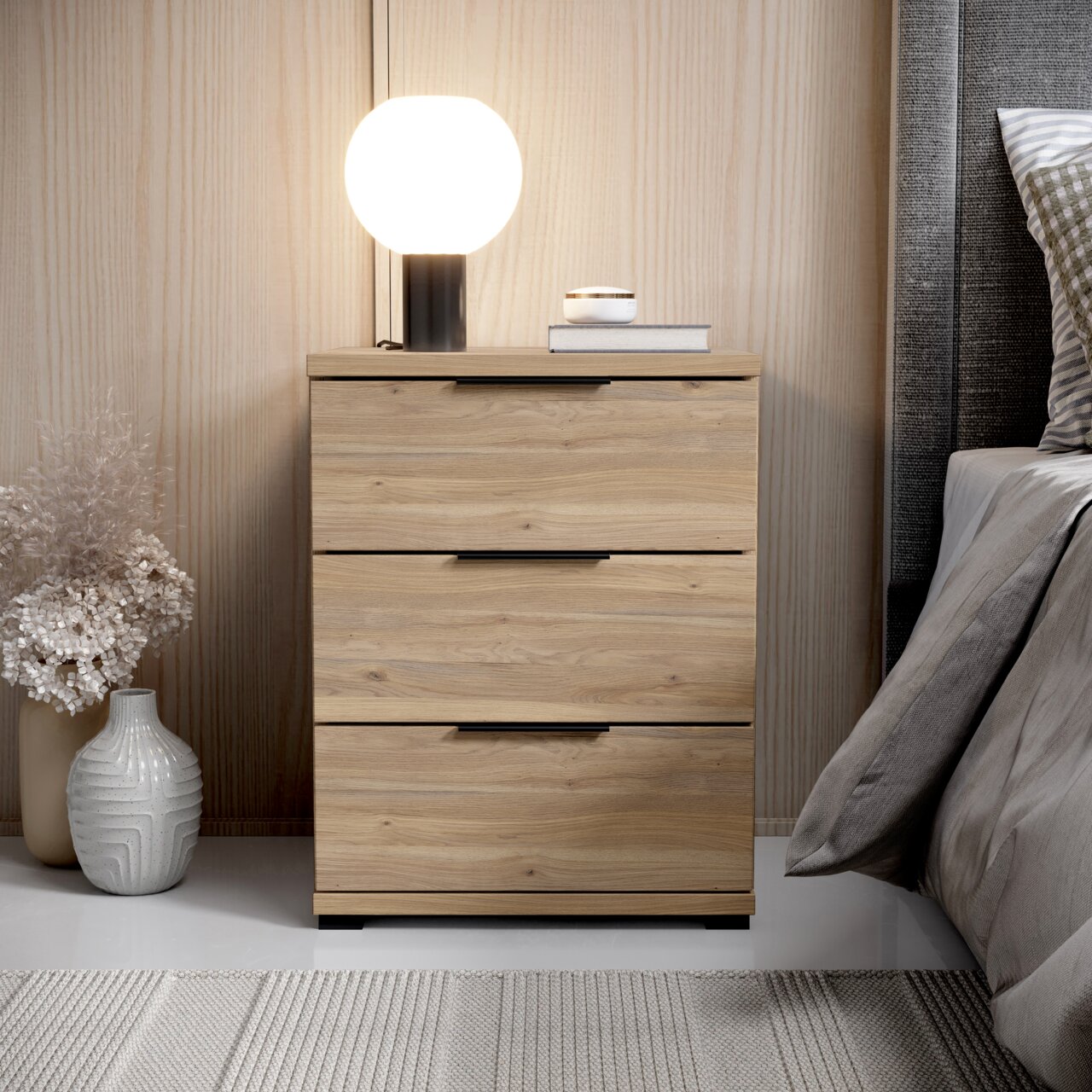 Z2 Nachtkommode SMILLA 2 Nachtkommode aus Holz mit drei Schubladen, darauf eine runde Lampe und Bücher, seitliche Perspektive