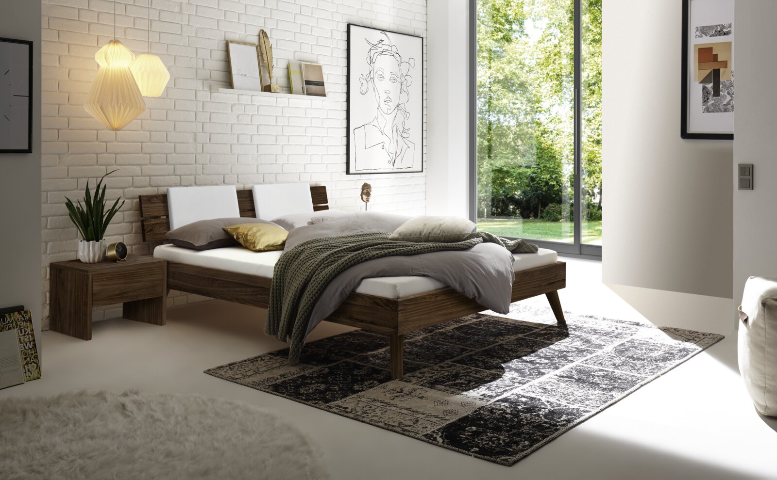 Modernes Schlafzimmer mit einem Kopfteil aus Holz und Metall, seitliche Perspektive. Das Bett ist mit weißen und grauen Kissen sowie einer grünen Decke dekoriert. Im Hintergrund sind eine weiße Ziegelwand und große Fenster zu sehen, die viel Tageslicht he