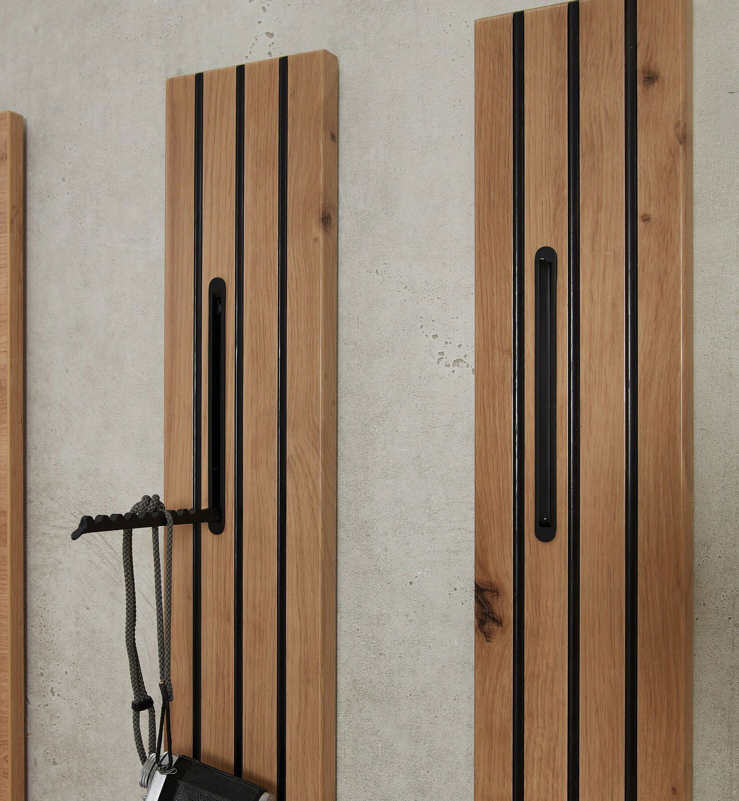 Zwei vertikale Garderobenpaneele aus Holz mit schwarzen Akzenten, an einer Betonwand montiert. Perspektive von vorne.