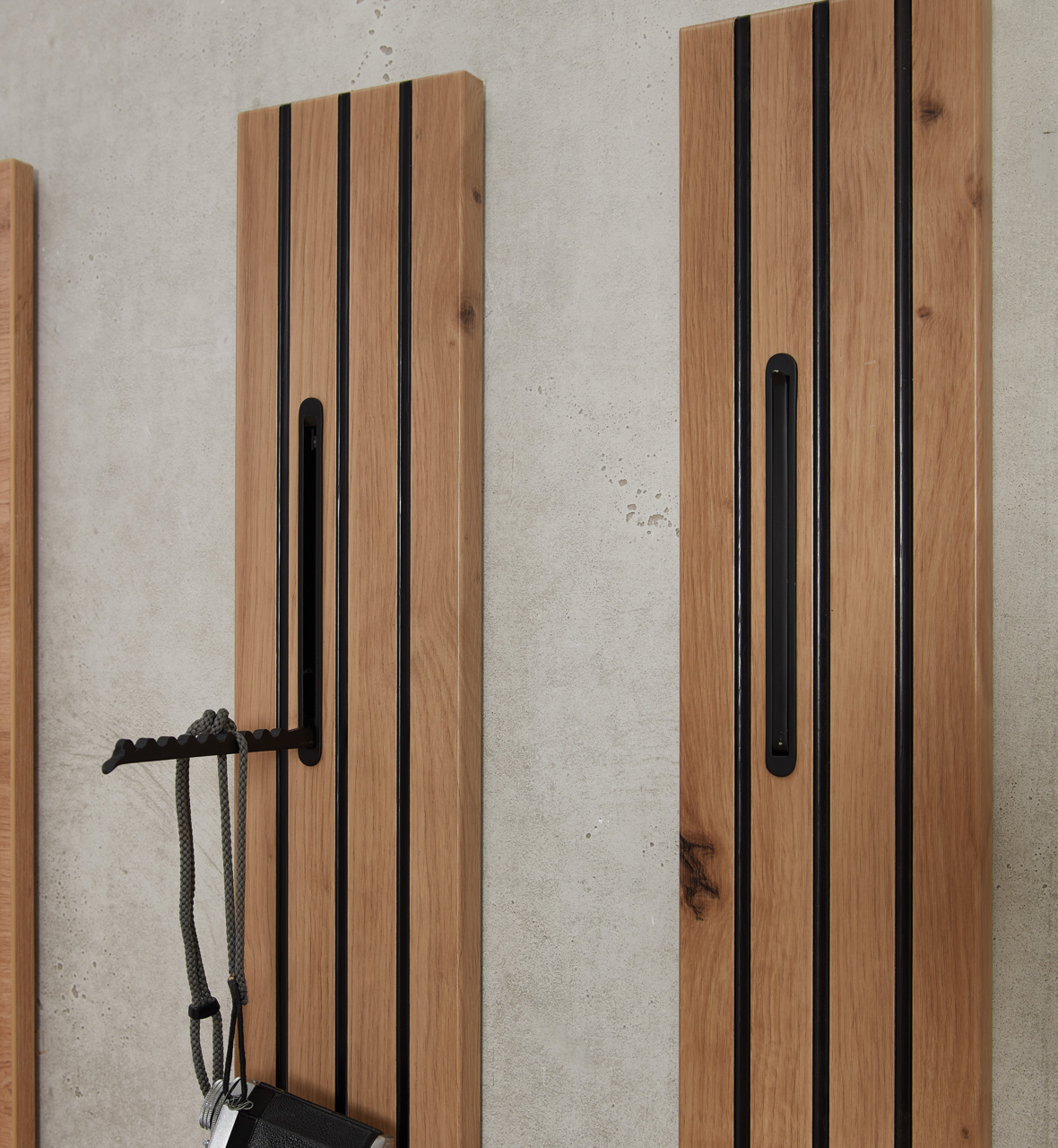 Zwei vertikale Garderobenpaneele aus Holz mit schwarzen Akzenten, an einer Betonwand montiert. Perspektive von vorne.