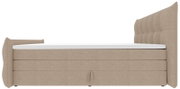 Beiges, gepolstertes Boxspringbett mit hohem, gestepptem Kopfteil und seitlichen Flügeln, mit weißer Matratzenauflage, Seitenansicht.