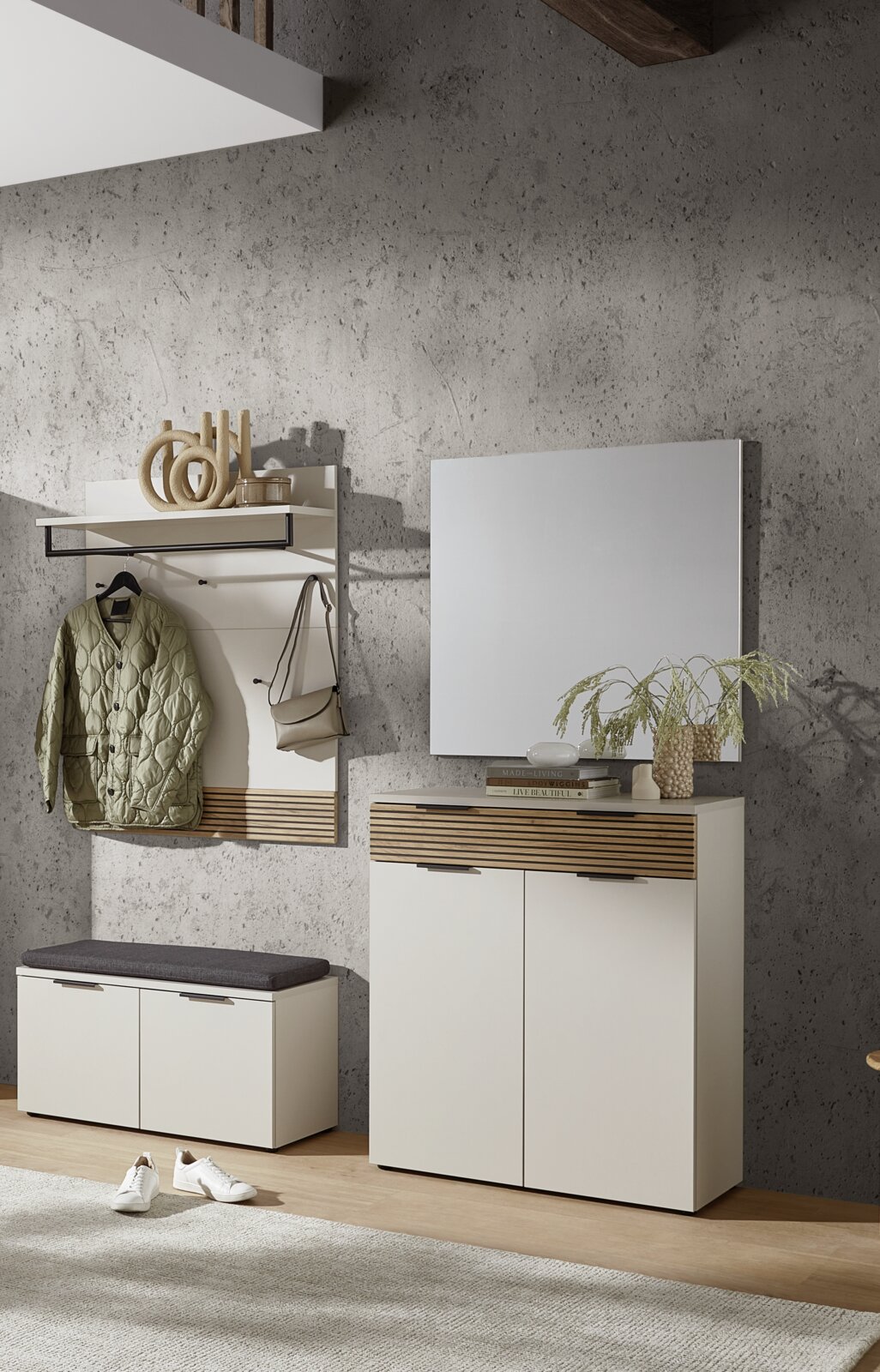 Voleo Garderoben-Set INDO Modernes Flurmöbel-Set in Weiß mit Holz-Lamellen-Akzenten: Wandgarderobe mit Ablage und Haken, Schuhbank mit grauem Sitzkissen, Schuhschrank mit Spiegel vor Betonwand, frontal in leichter Schrägansicht aufgenommen.