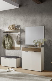 Modernes Flurmöbel-Set in Weiß mit Holz-Lamellen-Akzenten: Wandgarderobe mit Ablage und Haken, Schuhbank mit grauem Sitzkissen, Schuhschrank mit Spiegel vor Betonwand, frontal in leichter Schrägansicht aufgenommen.