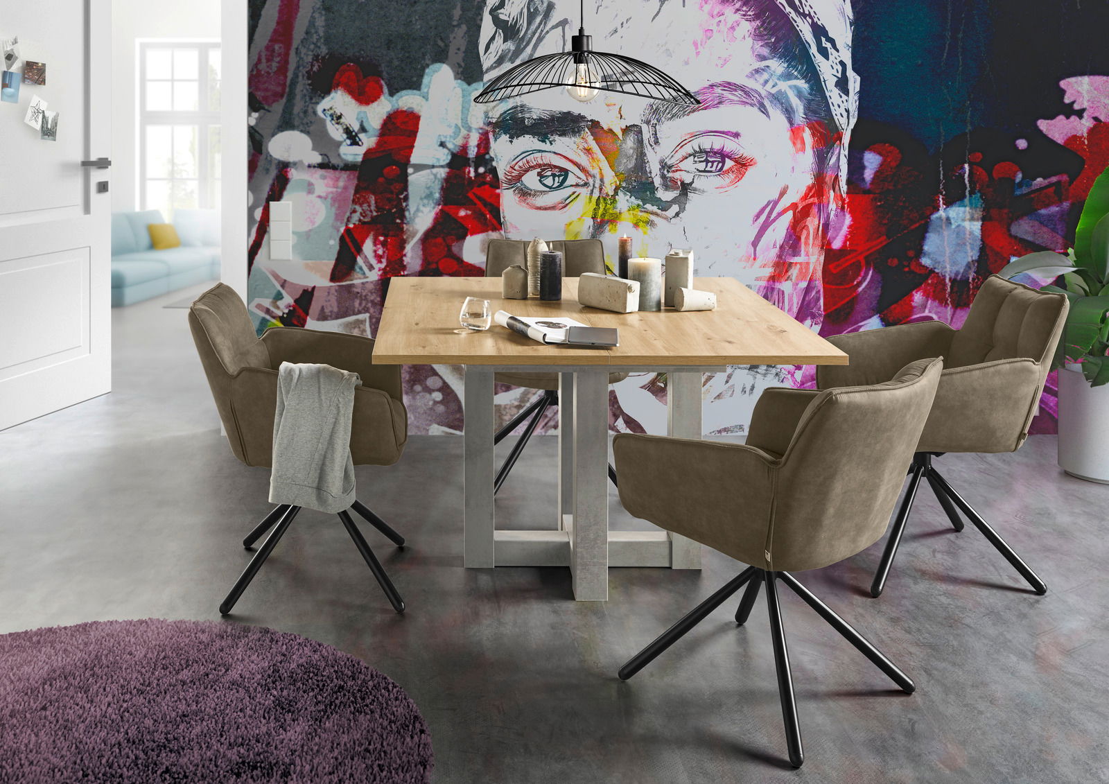 Set one by Musterring Armlehnstuhl FRISCO Esszimmer mit einem Holztisch und vier drehbaren Armlehnstühlen der Serie FRISCO von Set One by Musterring, vor einer bunten Wand mit Kunstmotiv. Perspektive: seitlich.