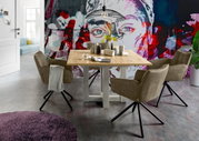 Esszimmer mit einem Holztisch und vier drehbaren Armlehnstühlen der Serie FRISCO von Set One by Musterring, vor einer bunten Wand mit Kunstmotiv. Perspektive: seitlich.