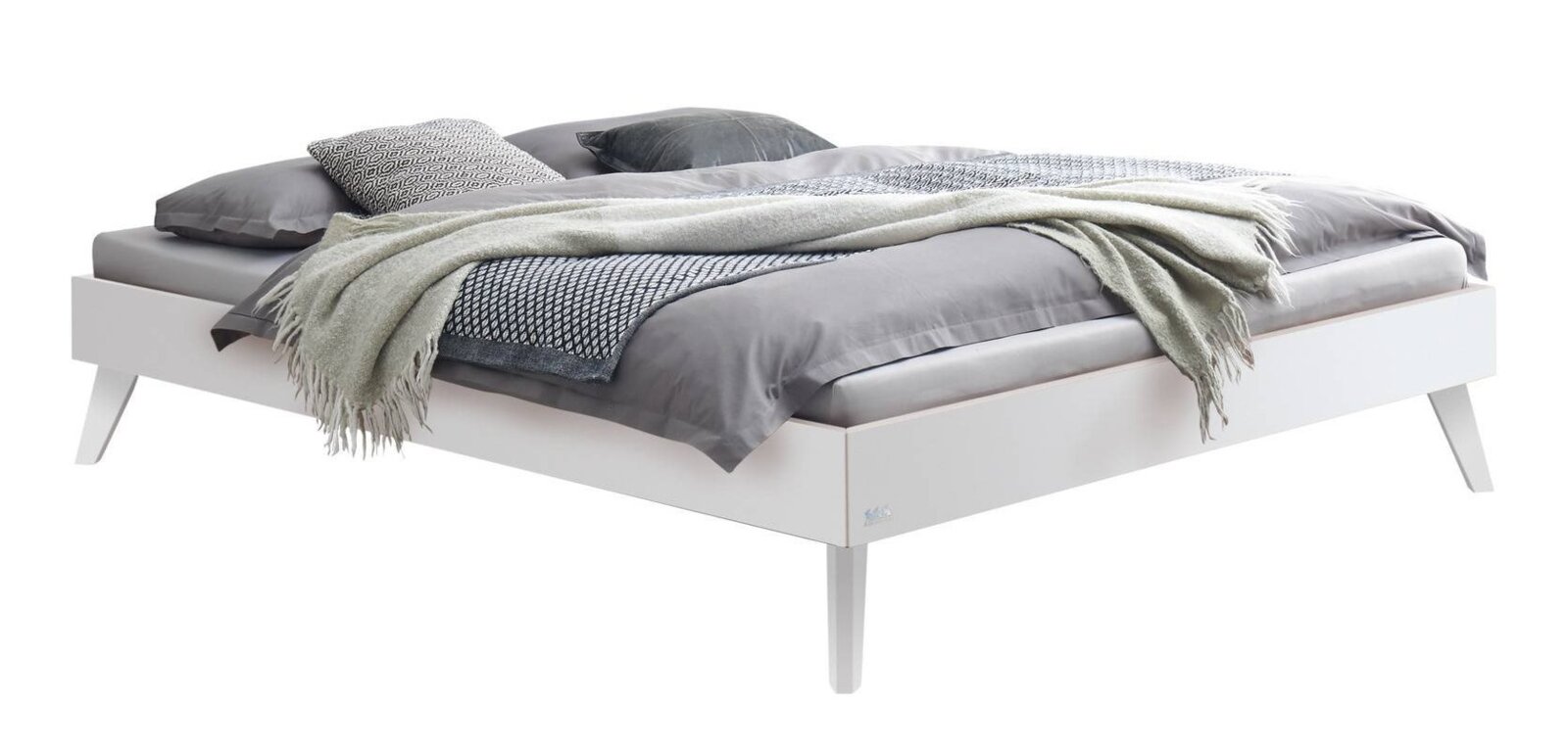 Modern wit bedframe met schuine poten, bekleed met grijs beddengoed, kussens en een deken schuin vooraanzicht/zijaanzicht tegen een witte achtergrond