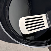 Nahaufnahme eines glänzenden schwarzen Schmortopfs mit einem silbernen Pfannenwender auf der Innenseite.