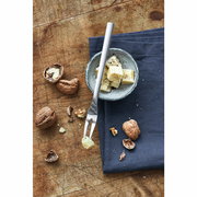 Serviergabel aus Edelstahl auf einem Holztisch, neben einer Schale mit Käsewürfeln und Walnüssen, aus der Vogelperspektive.